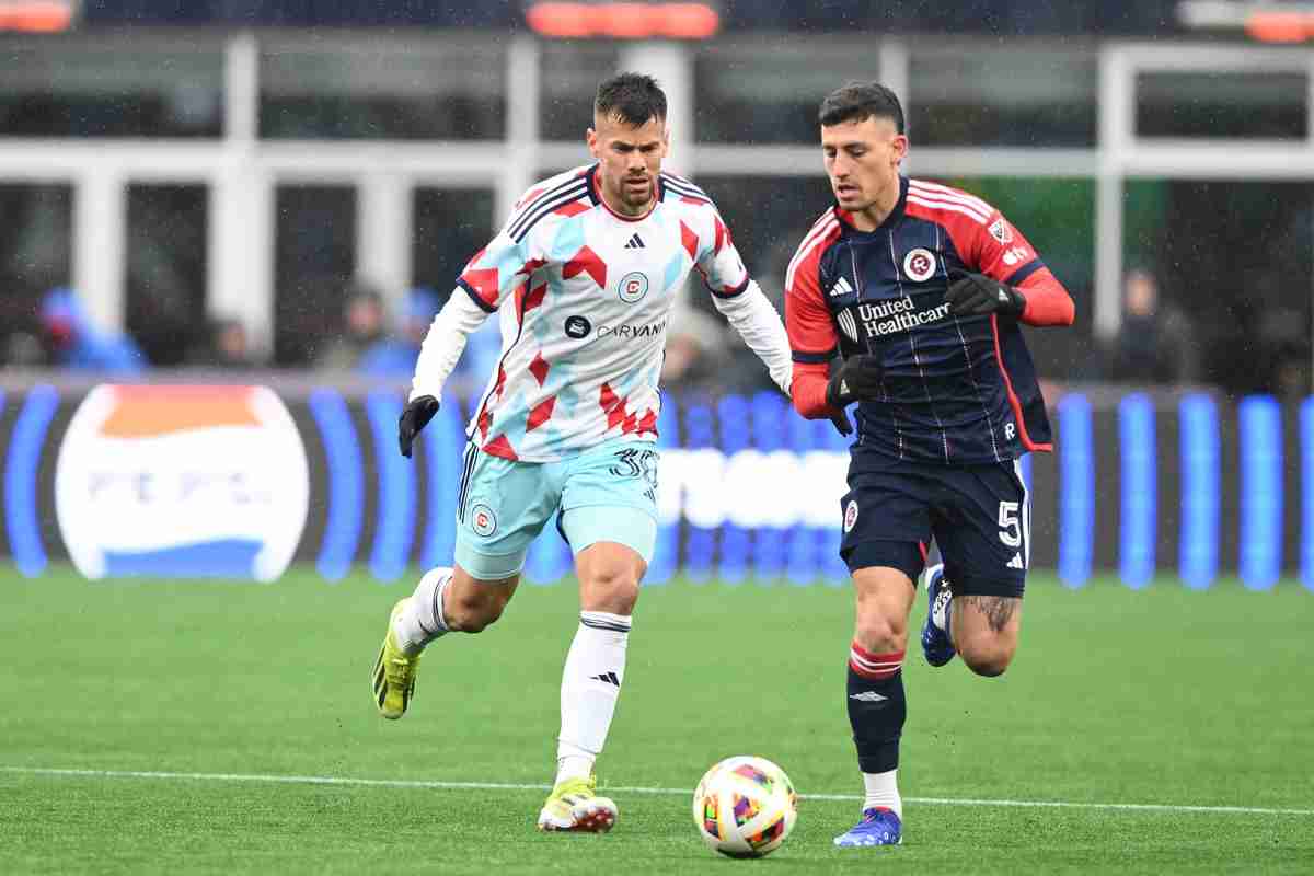 Two soccer players go for the ball during a rainy soccer game