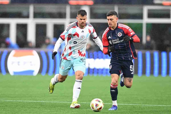 Two soccer players go for the ball during a rainy soccer game